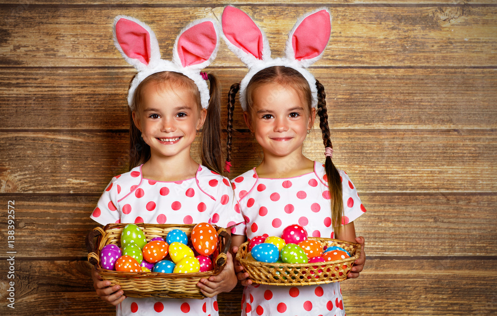 Happy easter! cute twins girls sisters dressed as rabbits with eggs on wooden background