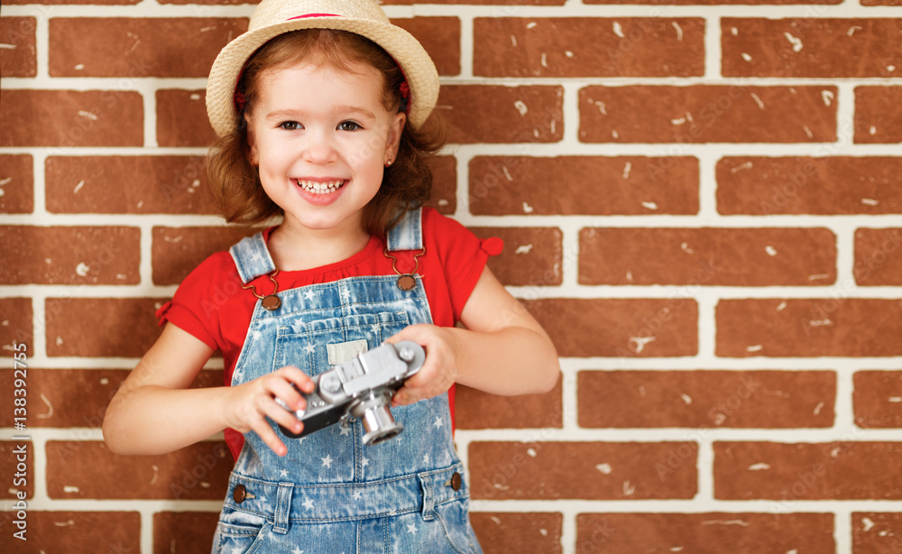 Happy child girl photographer with camera at brick wall