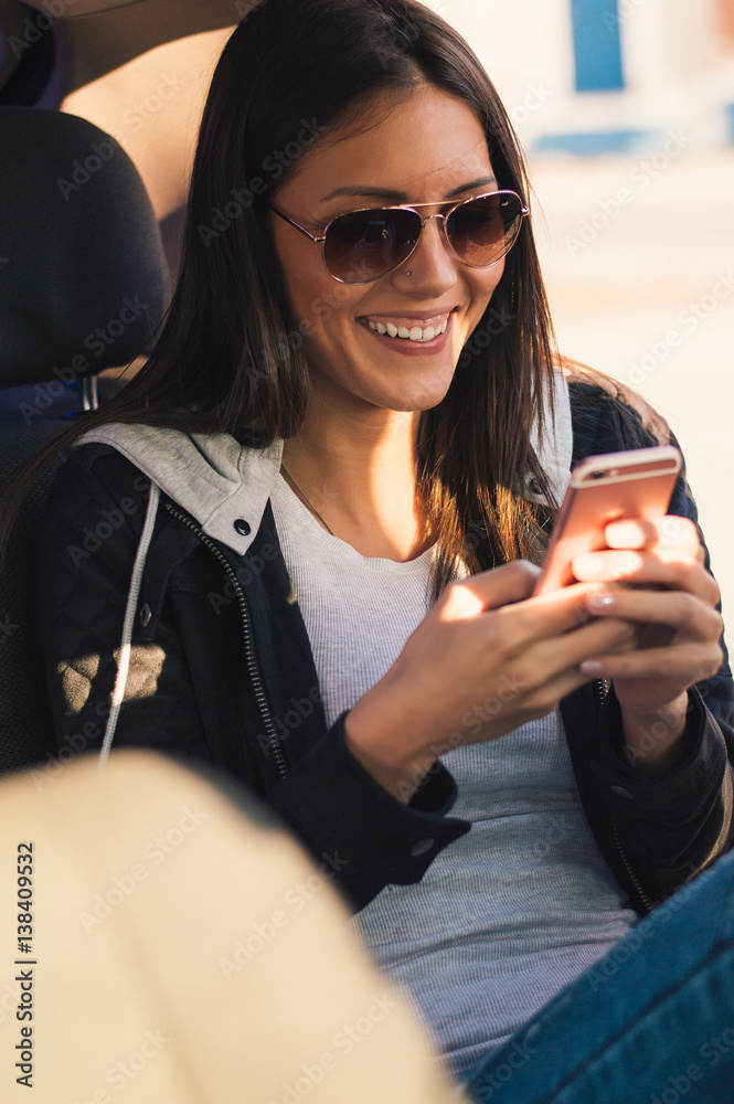 Young business woman in a taxi. She is watching something on her smart phone