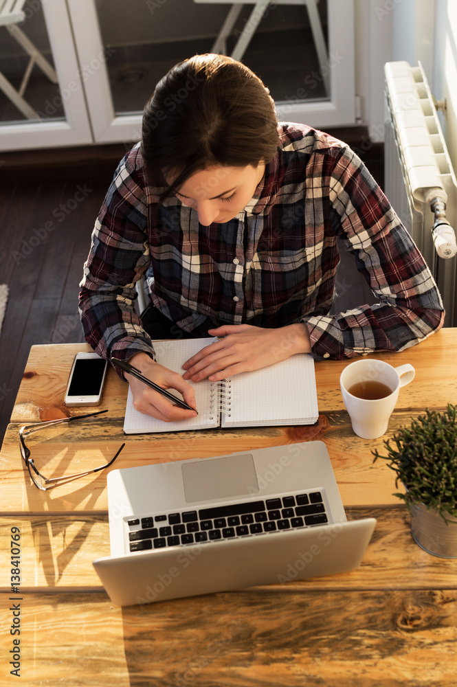 Young woman working in home office. Student writing report