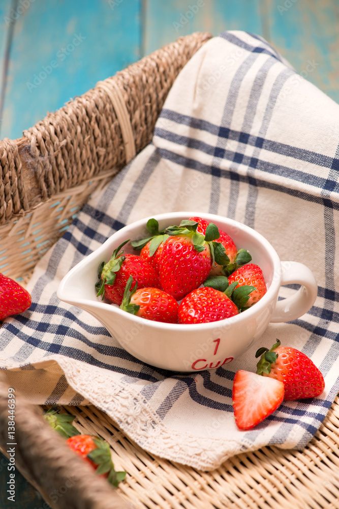 Bowl with fresh strawberry on blue wooden table.