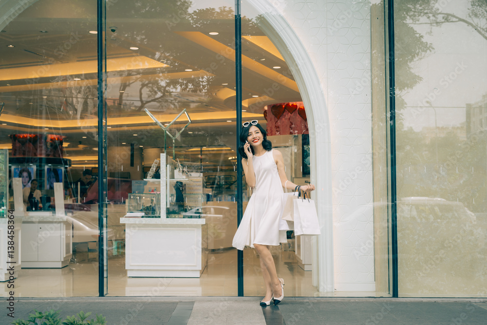 Beautiful asian girl with shopping bags listening to mobile phone standing outside the mall