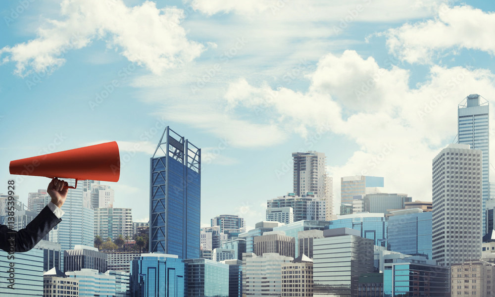 Hand of businesswoman holding red paper trumpet against cityscape background