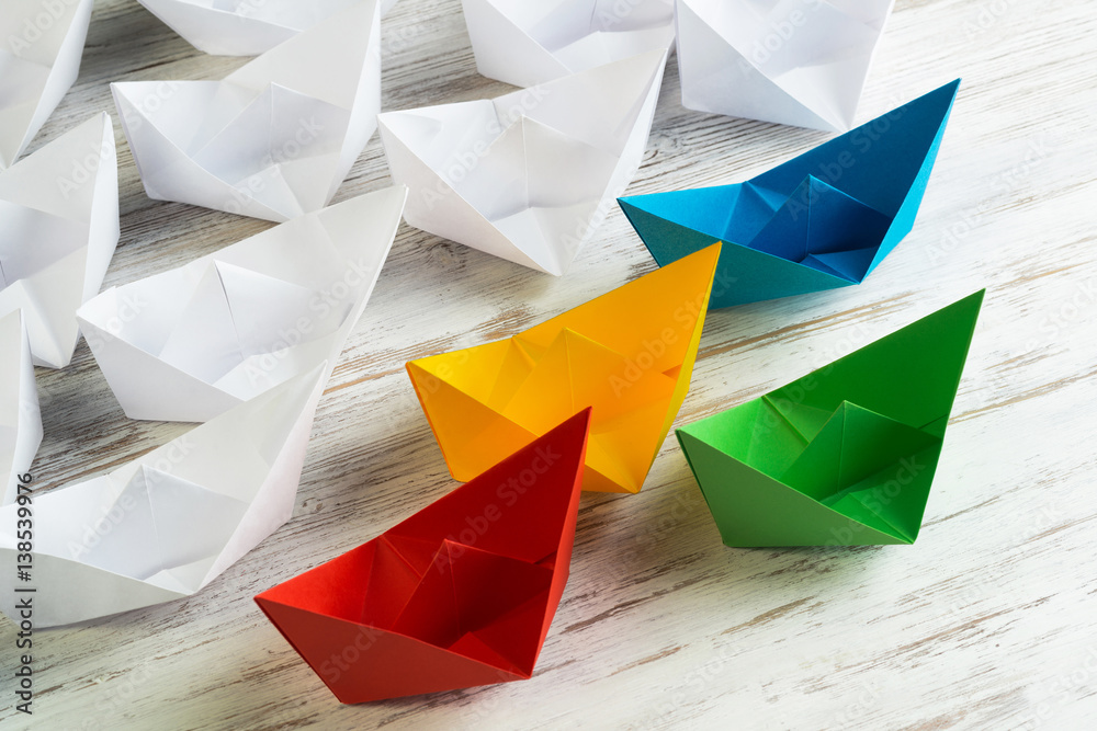 Business leadership concept with white and color paper boats on wooden table