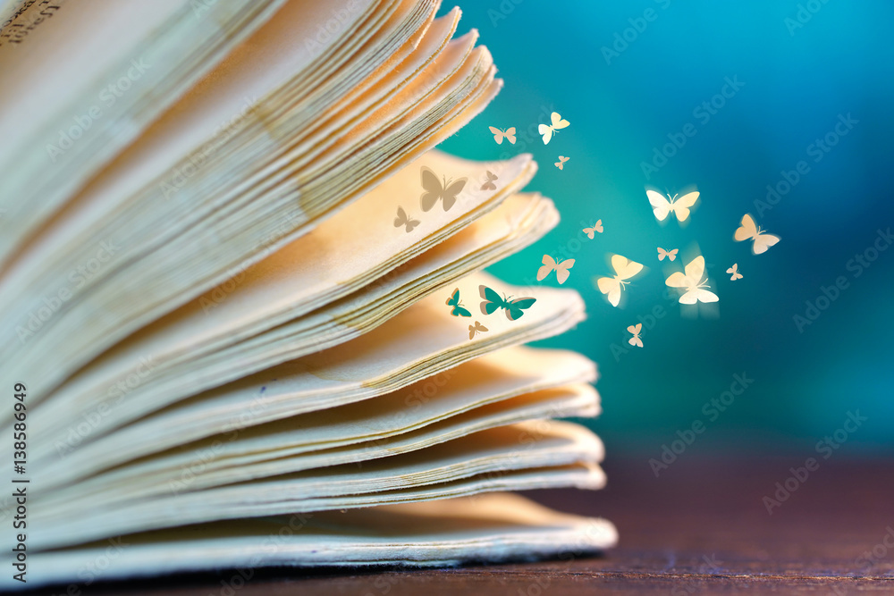 Open old book on a wooden table close-up macro and departing from the pages of paper butterflies on 