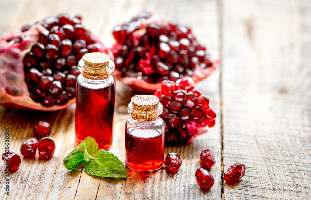 sliced pomegranate and extract in glass on wooden background