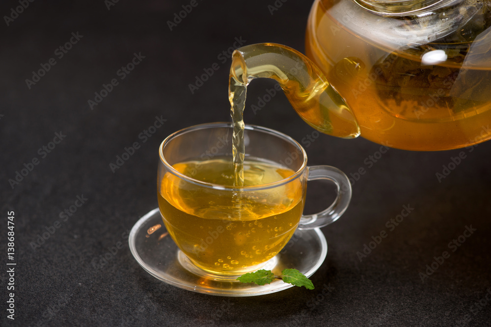 Pouring tea. Cup of hot tea and tea leaf on black stone background.