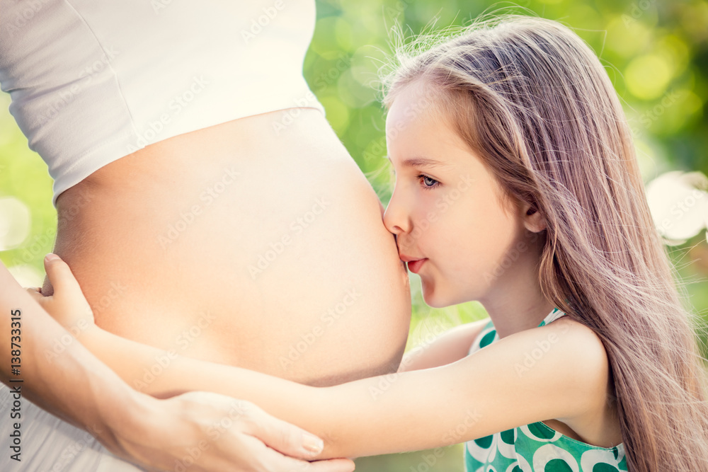 Happy child kissing belly of pregnant woman