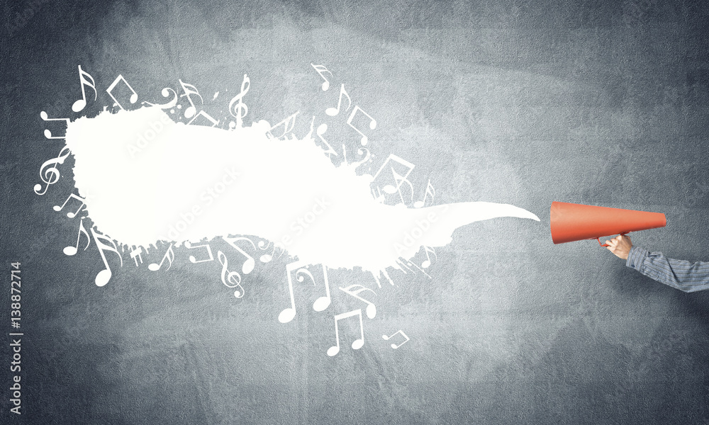 Hand of man holding orange paper trumpet against concrete background