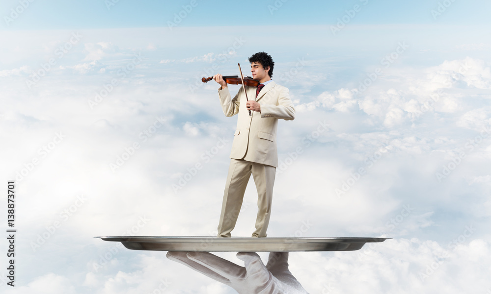 Businessman on metal tray playing violin against blue sky background