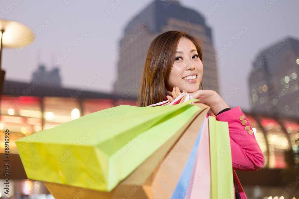 年轻的亚洲女人在城市街道上拿着购物袋