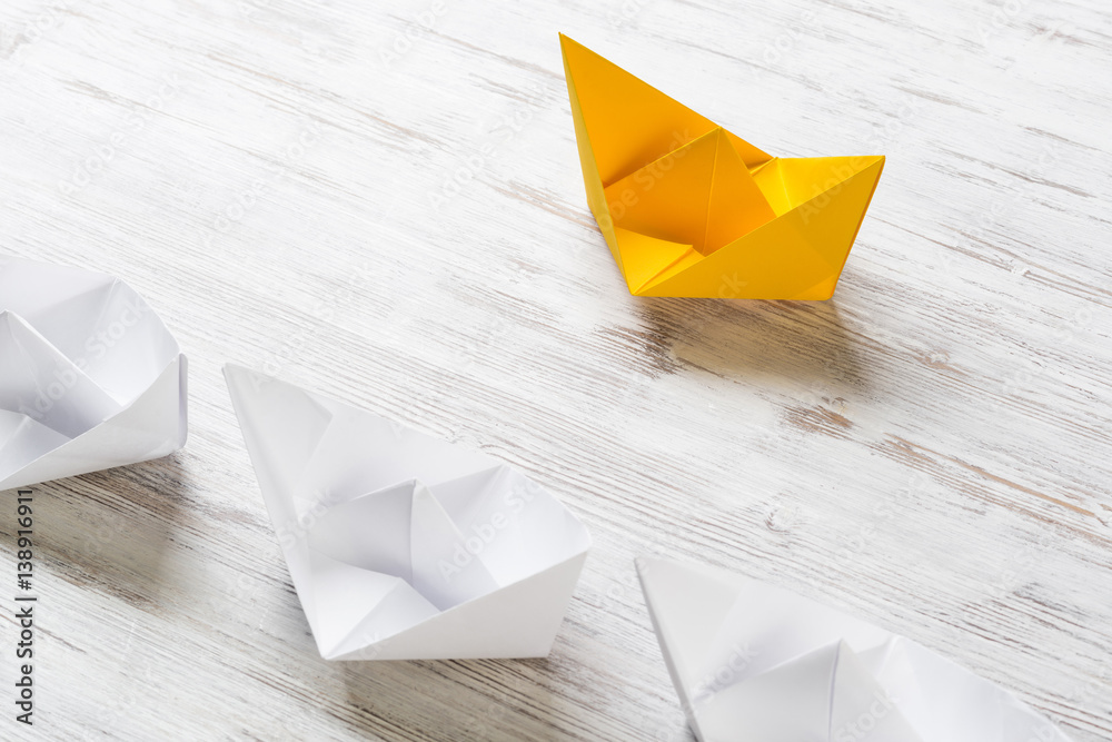 Business leadership concept with white and color paper boats on wooden table