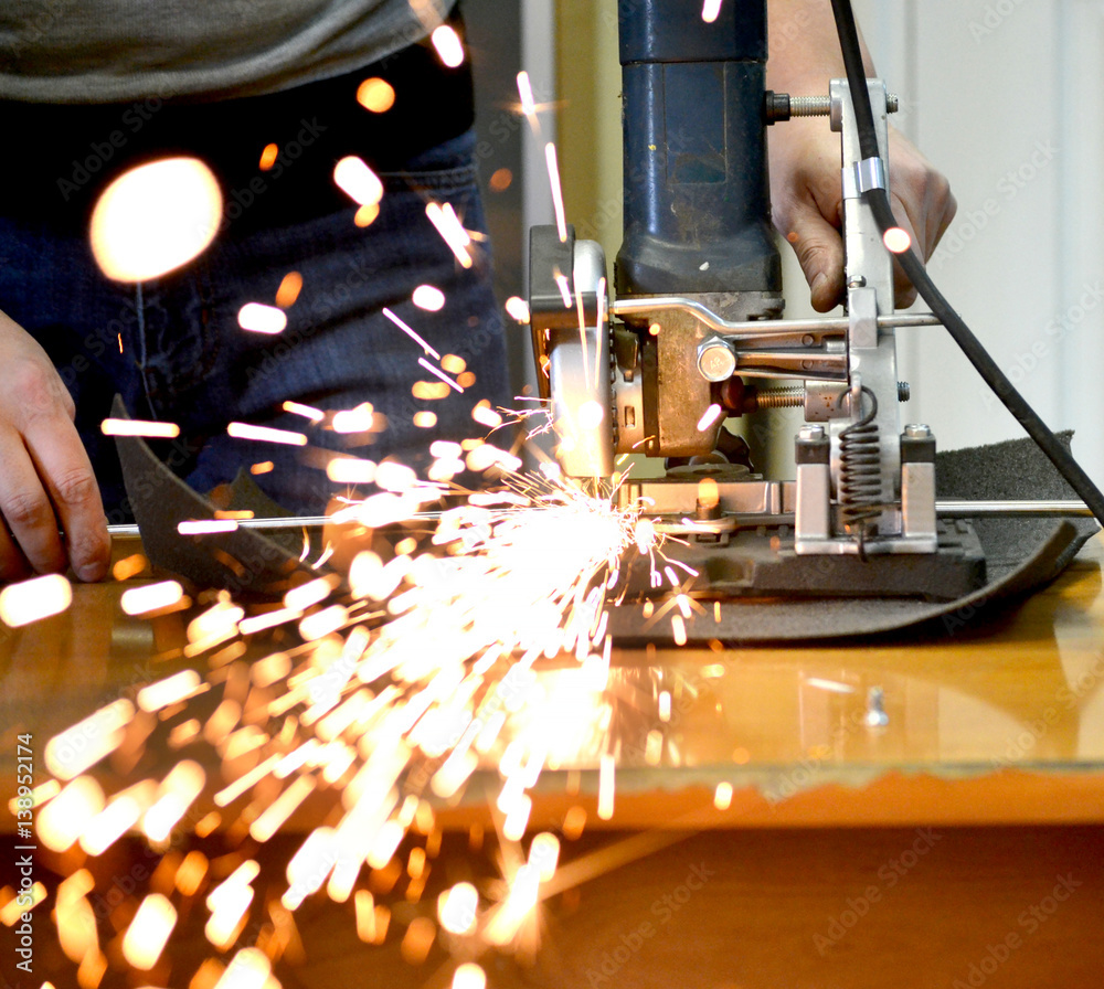 Worker man cutting a metal pipe in two pieces and lot of sparks flying straight into the camera clos