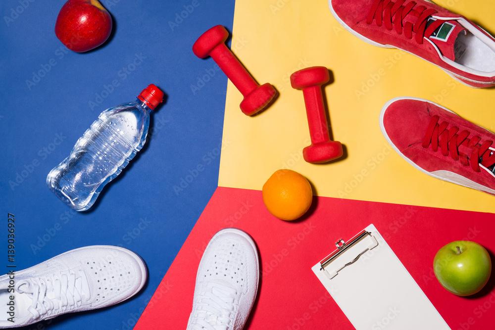 Sport concept. Fitness equipment. Sneakers, water, apple, dumbbell on colorful background.