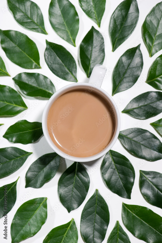 Flat lay of green leaves pattern with cup of coffee on white background