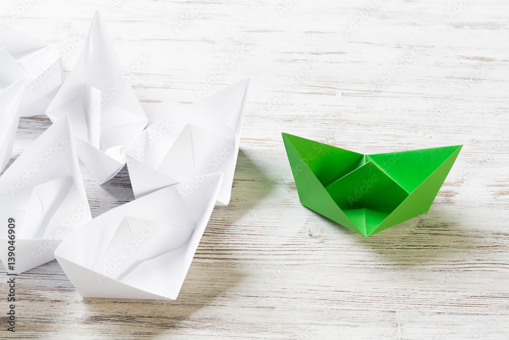 Business leadership concept with white and color paper boats on wooden table