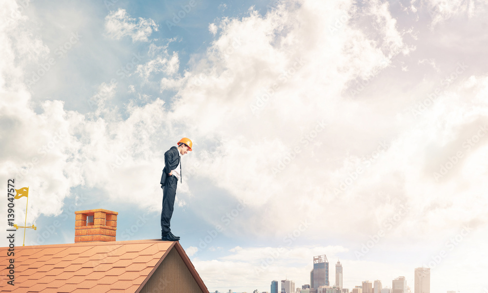 Businessman looking down from roof and modern cityscape at backg