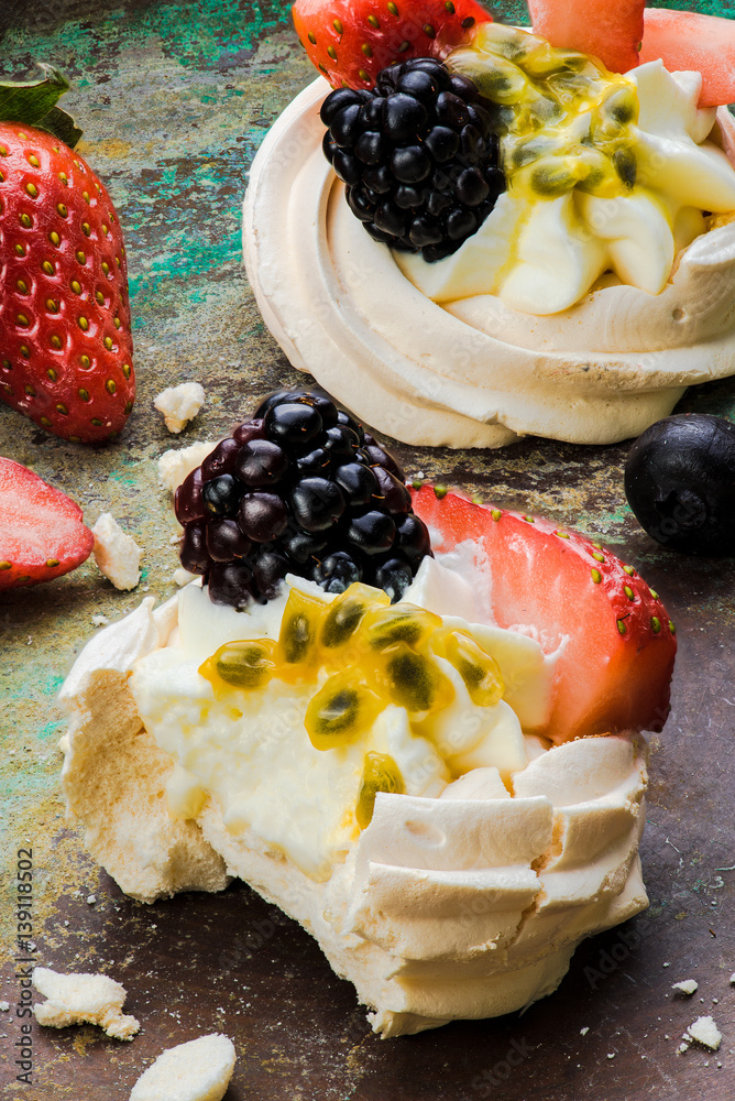 Mini Pavlova meringue cakes with berries and passion fruits on rustic vintage background. Top view.