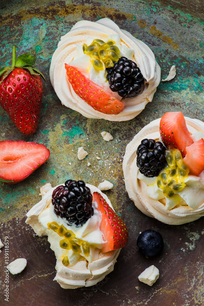 Mini Pavlova meringue cakes with berries and passion fruits on rustic vintage background. Top view.