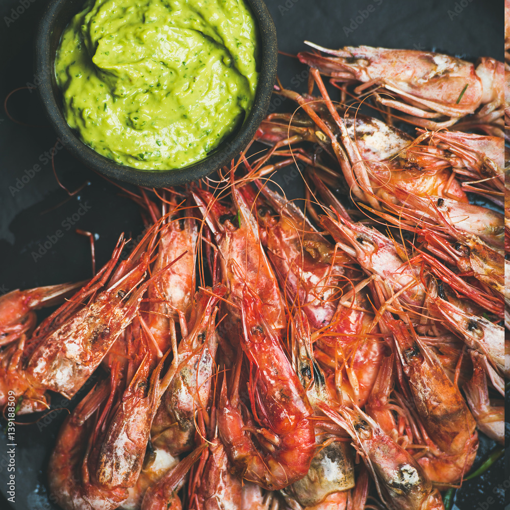 Roasted red shrimps with guacamole avocado sauce in slate stone black plate over grey concrete backg