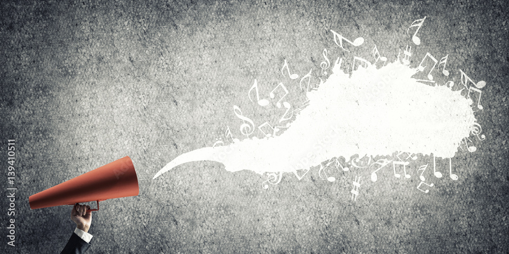 Hand of businesswoman holding red paper trumpet against concrete background