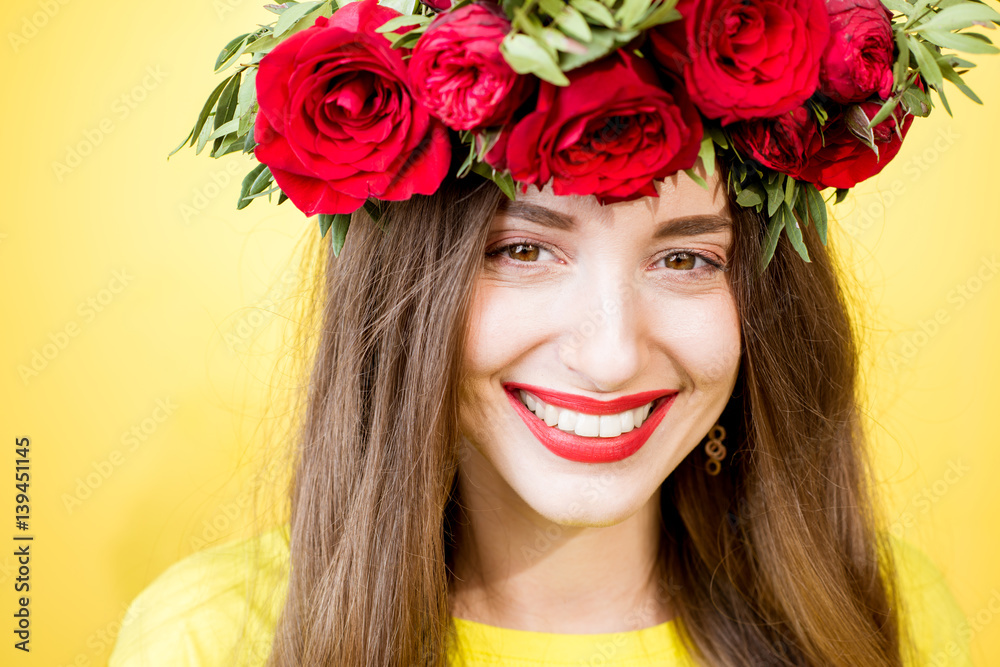 Close-up portrait of a beautiful woman with wreath made of red roses on the yellow background