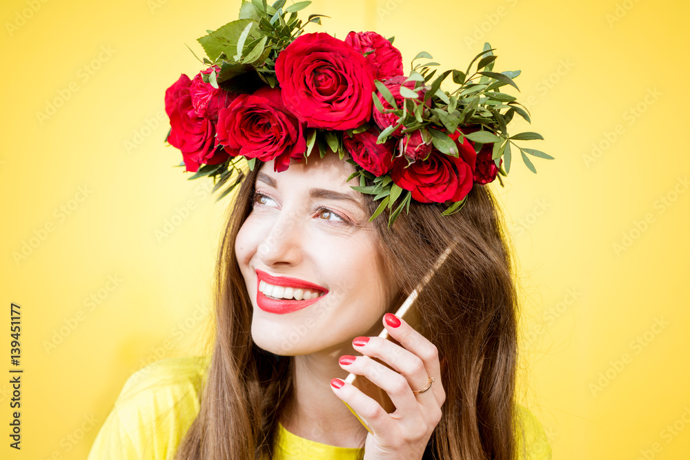 Close-up portrait of a beautiful woman with wreath made of red roses talking with phone on the yello