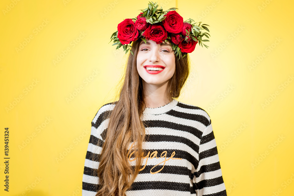 Colorful portrait of a beautiful woman in sweater with wreath made of red roses on the yellow backgr