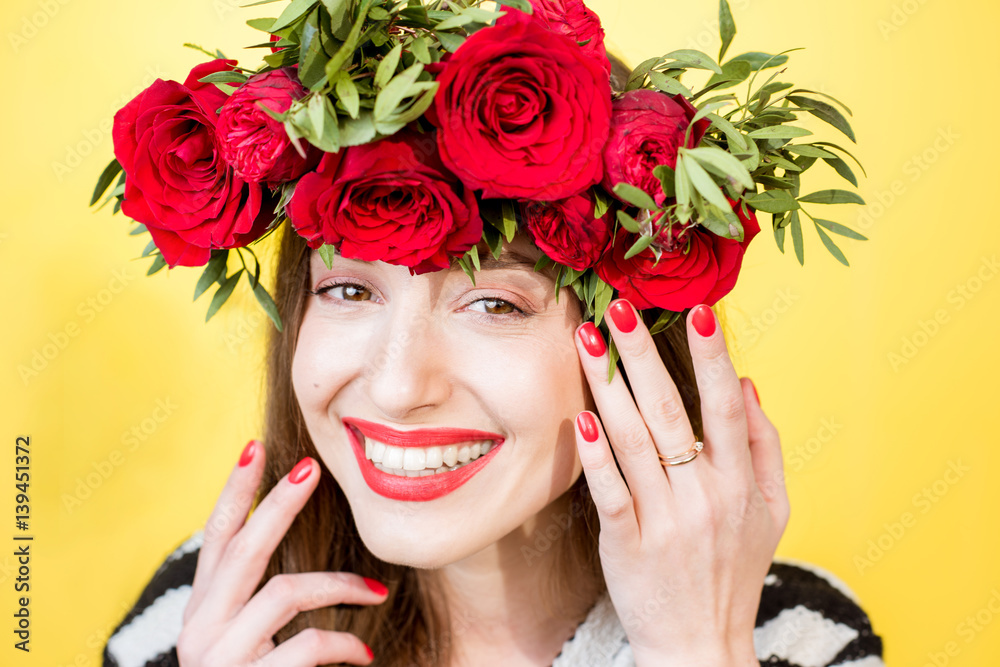 Close-up portrait of a beautiful woman in sweater with wreath made of red roses on the yellow backgr