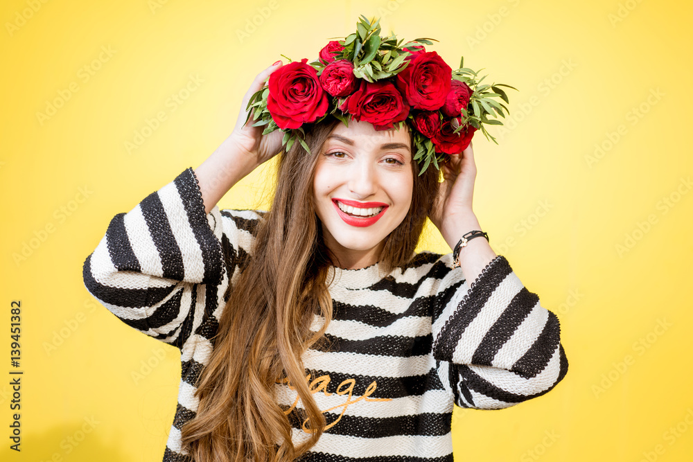 Colorful portrait of a beautiful woman in sweater with wreath made of red roses on the yellow backgr