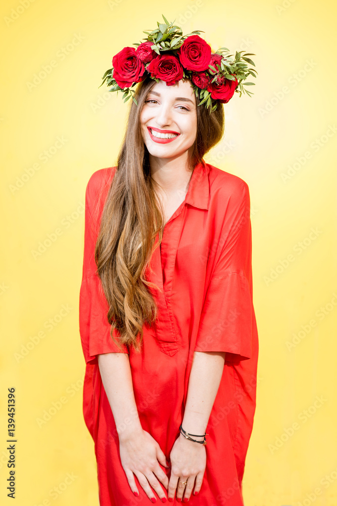 Colorful portrait of a beautiful woman in red dress with wreath made of red roses on the yellow back