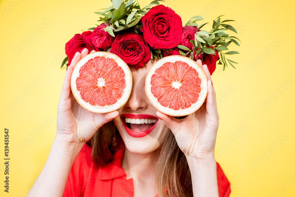 Colorful portrait of a beautiful woman with flower wreath holding slices of grapefruits on the yello