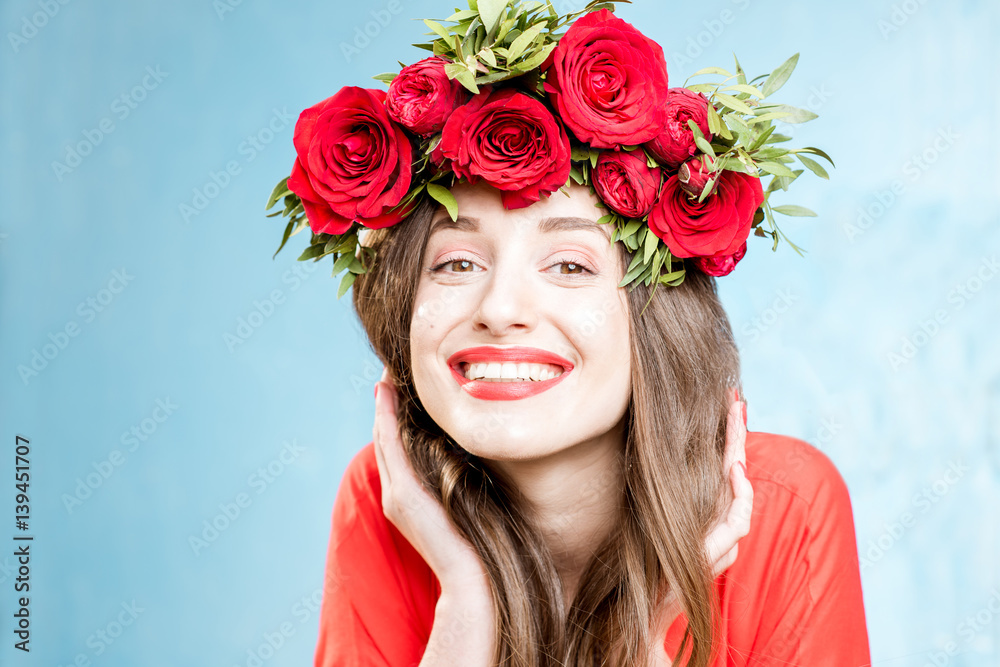 Colorful portrait of a beautiful woman in red dress with wreath made of red roses on the blue backgr