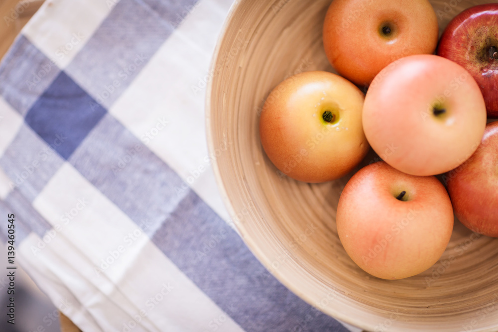 red apple in wooden bowl on color checker fabric with moring light on wooden table