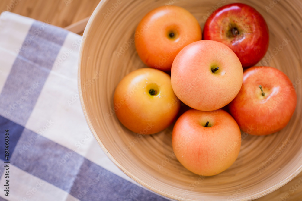 red apple in wooden bowl on color checker fabric with moring light on wooden table