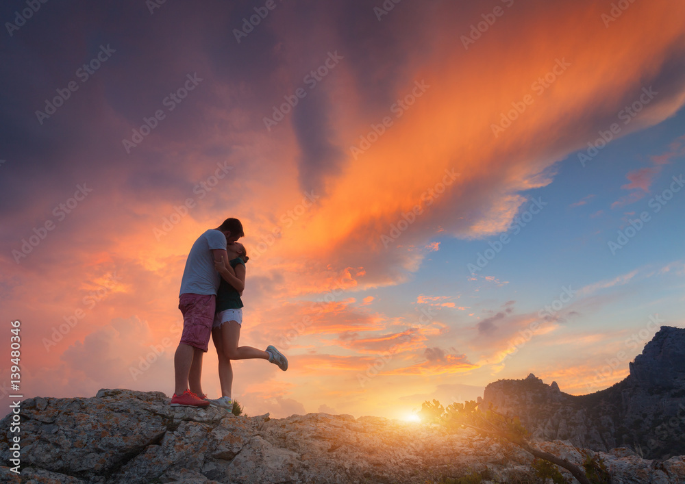 Silhouettes of a hugging and kissing man and girlfriend on the mountain peak at sunset. Man and woma