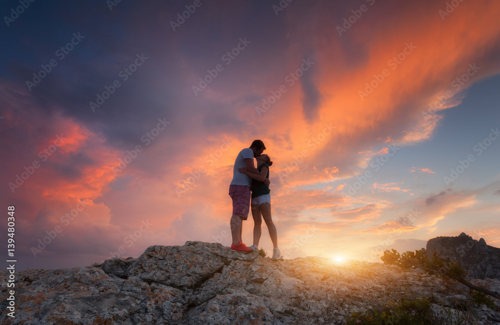 日落时，一对男女在山峰上拥抱亲吻的剪影。带si的风景