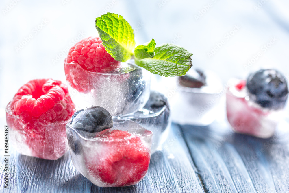 fresh berries with mint in ice cubes on wooden background