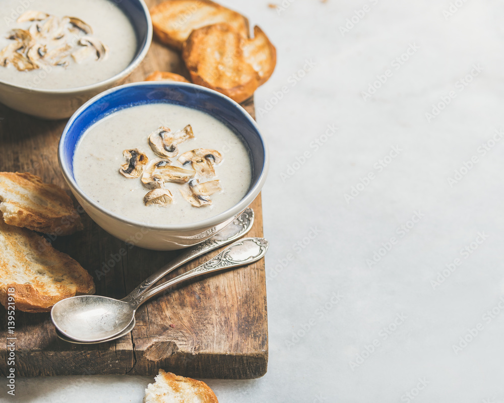 Healthy dinner with creamy mushroom soup in bowls and grilled bread slices on rustic serving board o