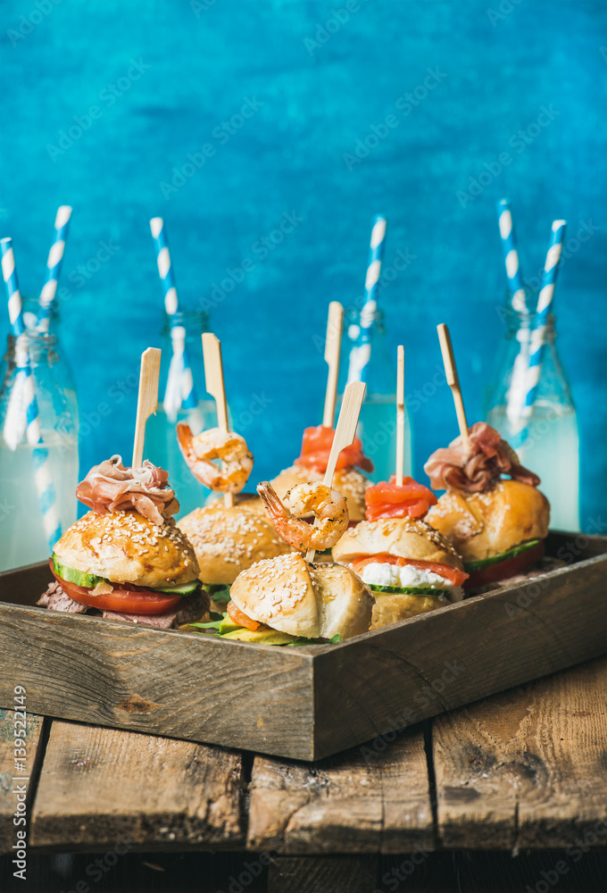 Home party food concept. Homemade burgers in wooden tray and lemonade in bottles with straws on rust