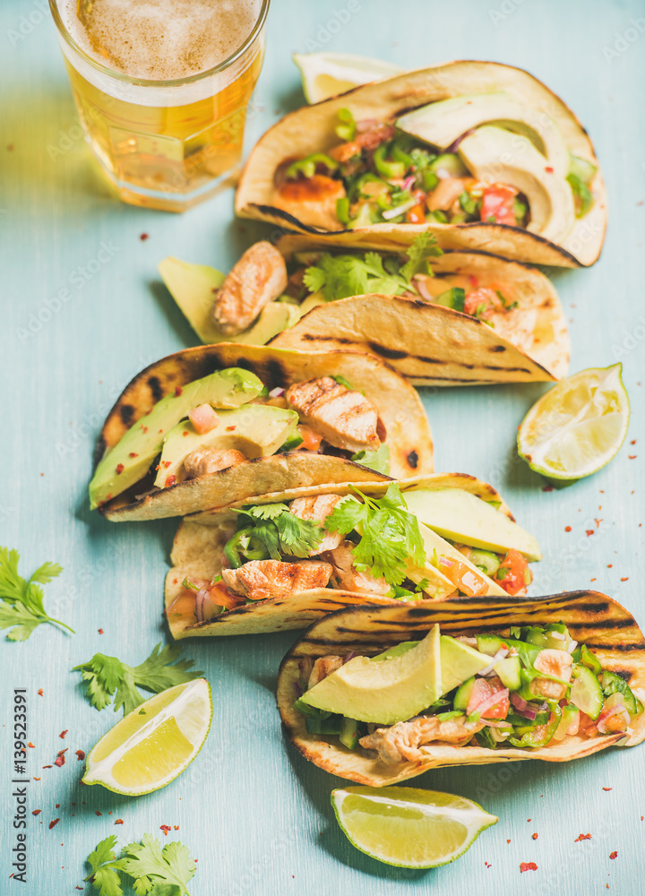 Healthy corn tortillas with grilled chicken, avocado, fresh salsa, limes and beer in glass over blue