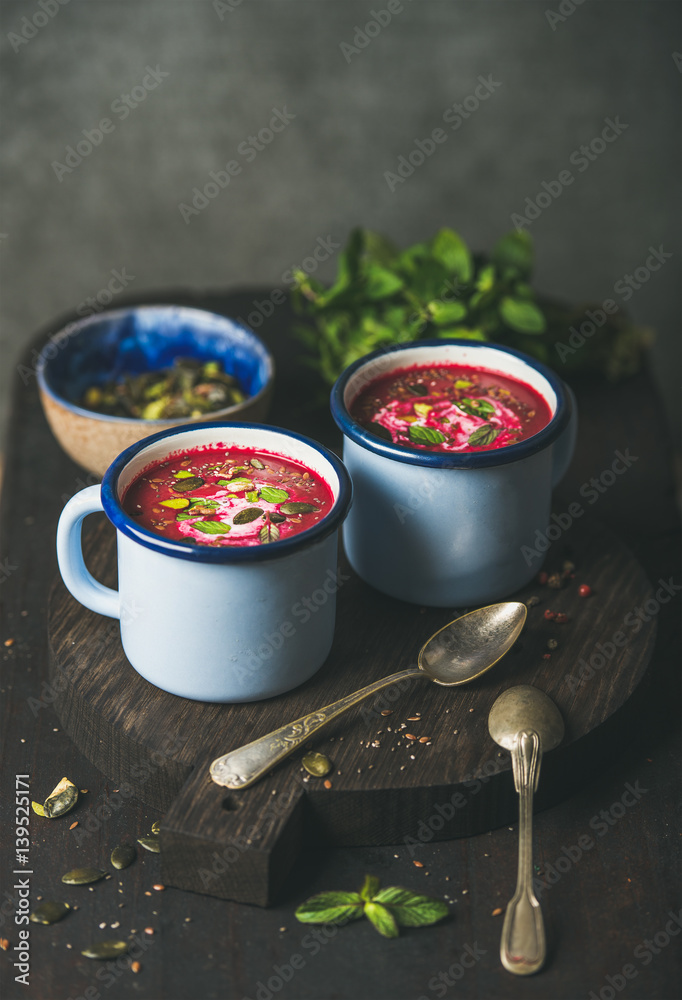 Spring beetroot soup with mint, pistachio, chia, flax, pumpkin seeds in blue enamel mugs over dark w