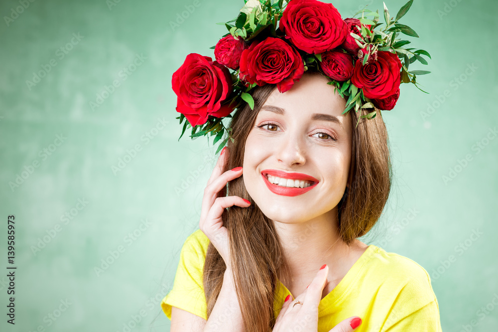 Colorful portrait of a beautiful woman in yellow t-shirt with wreath made of red roses on the green 