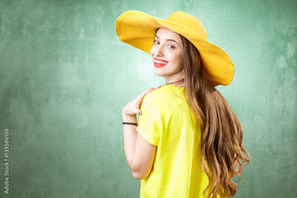 Colorful portrait of a beautiful woman in yellow t-shirt and hat on the green background