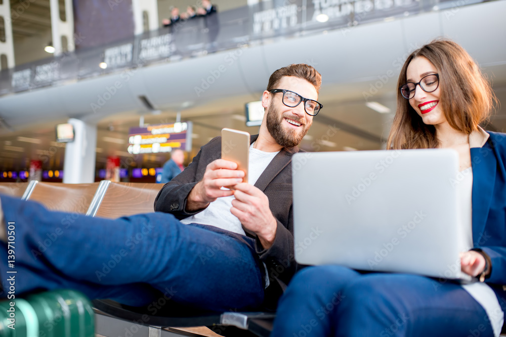 Elegant business couple working with laptop and phone sitting at the waiting hall in the airport. Bu