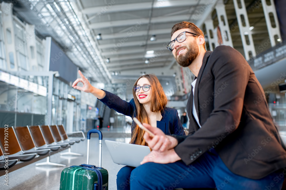 Elegant business couple sitting with laptop and baggage at the waiting hall in the airport. Having a