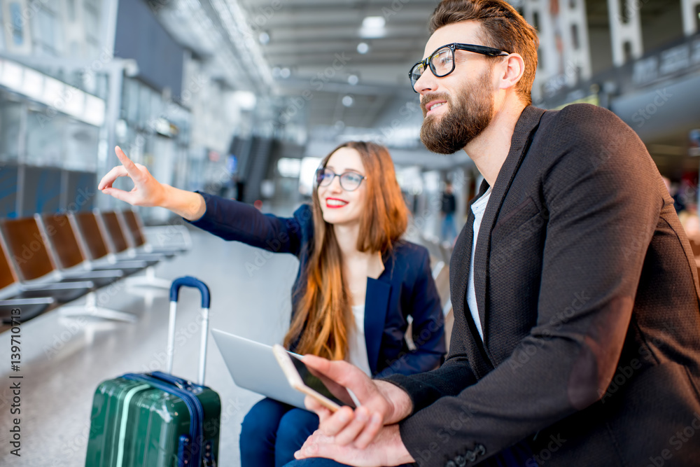 Elegant business couple sitting with laptop and baggage at the waiting hall in the airport. Having a