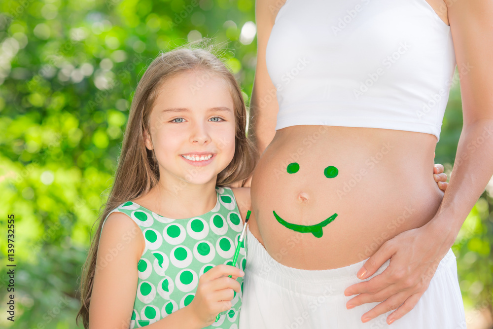 Happy child painting smile on belly of pregnant woman