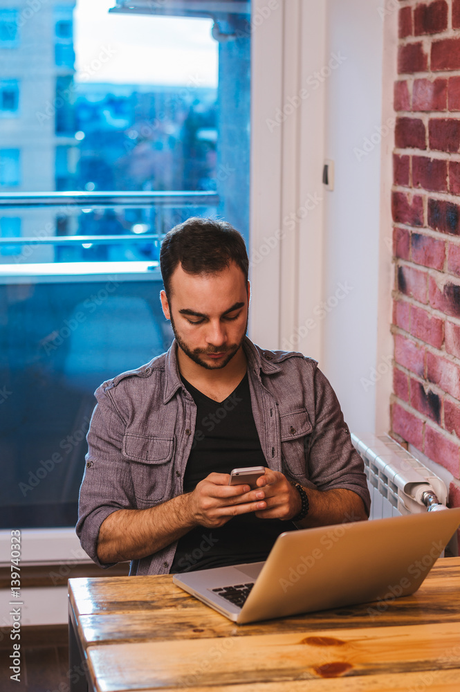 Young businessman working in the office while reading a message on his smartphone