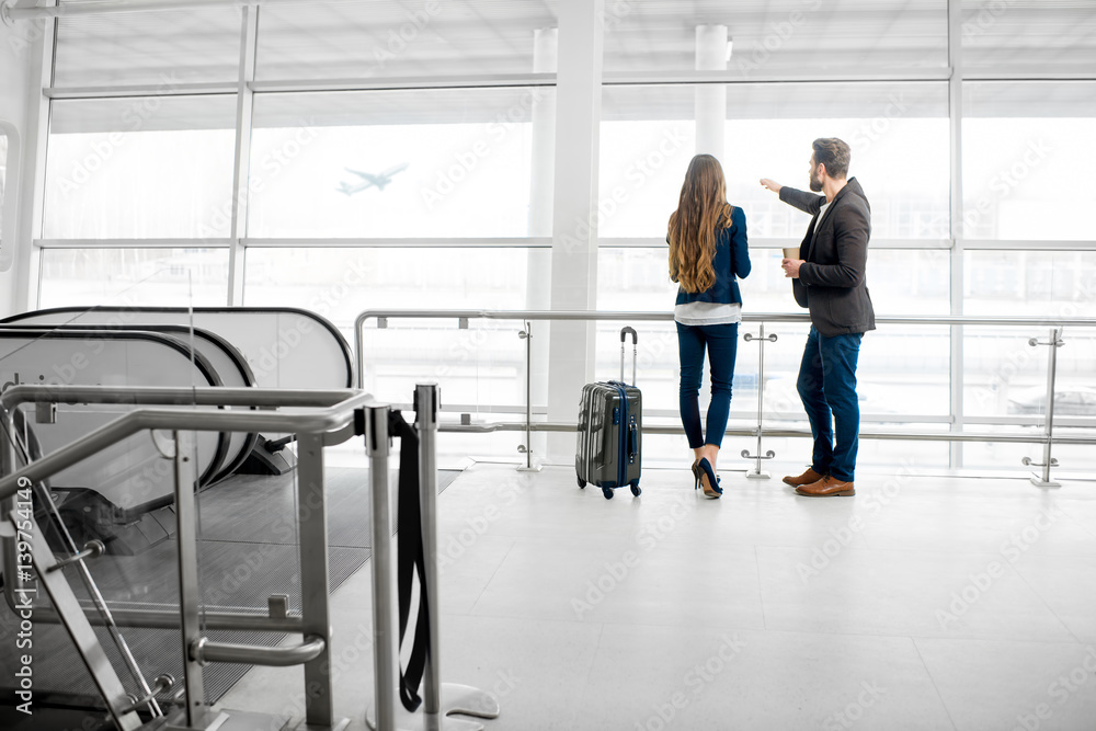 Business couple standing together with baggage near the window at the departure area at the airport